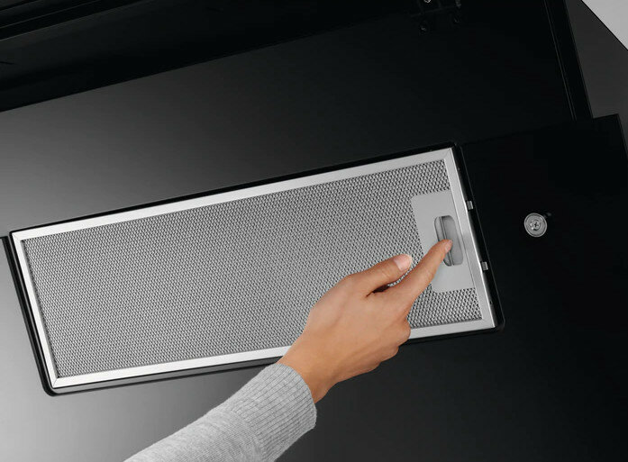 Ręka osoby próbującej wyjąć filtr z czarnego okapu, zbliżenie.