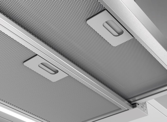 Zbliżenie na dwa metalowe filtry siatkowe z uchwytami do okapu kuchennego.