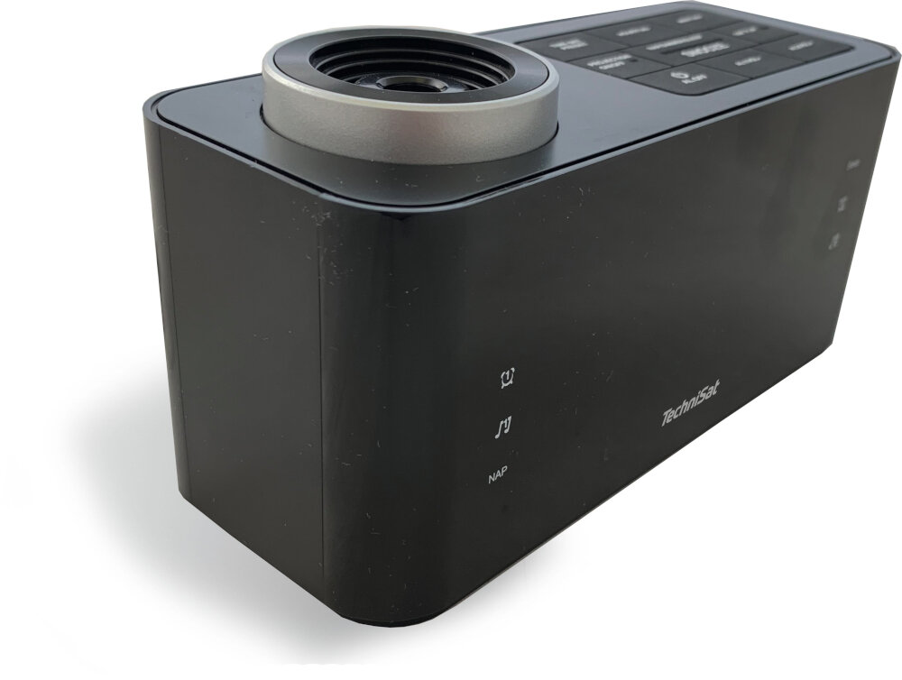 Czarny radiobudzik TechniSat ze srebrnym pierścieniem na górze i przyciskami na górze. Znajduje się na białej powierzchni.