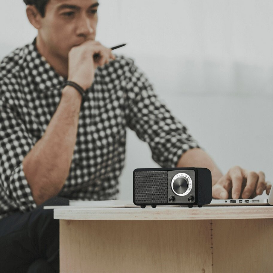 Mężczyzna siedzi przy stole, radio z przodu. Na stole laptop.