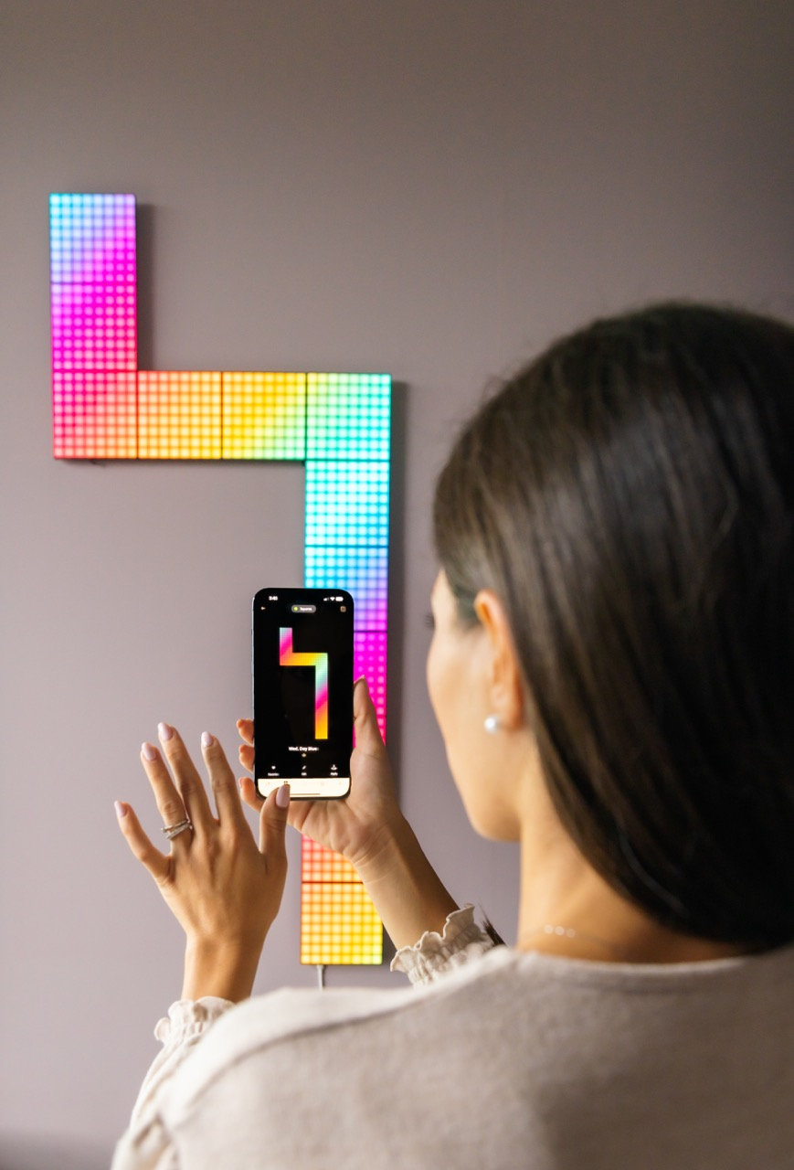 Donna che tiene un telefono, interagendo con un muro di piastrelle LED colorate.