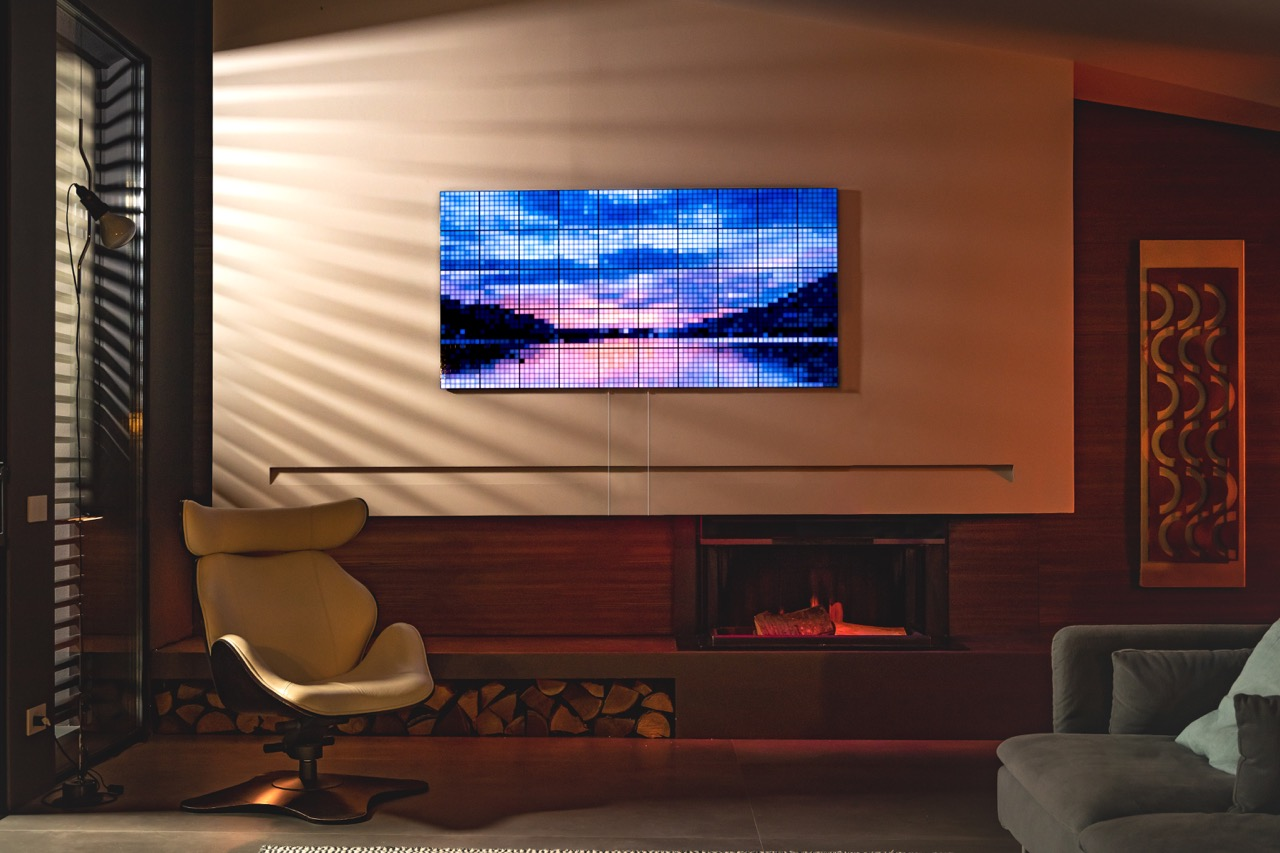 Soggiorno con TV che mostra un paesaggio. Sono visibili una sedia, un camino e una finestra. L'illuminazione è calda e ambiente.