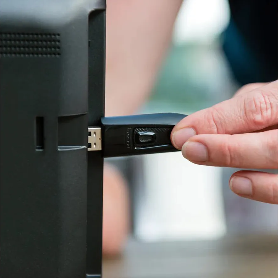 Una mano inserisce un dispositivo USB nero in una TV nera. La scena è in primo piano.