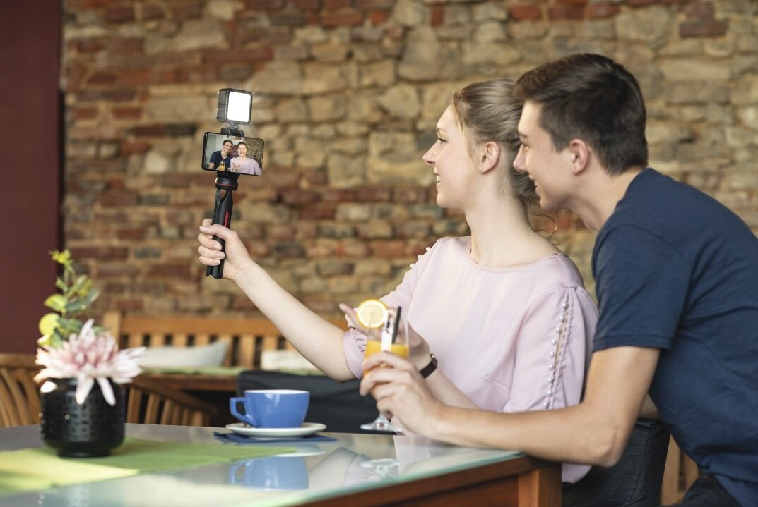 Para robiąca selfie w kawiarni, trzymająca telefon.
