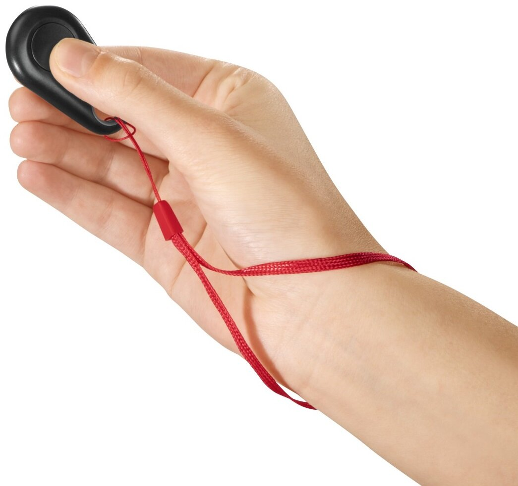 Dłoń trzymająca czarny lokalizator kluczy z czerwonym paskiem na nadgarstek.