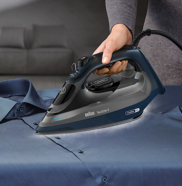 Osoba prasująca niebieską koszulę niebiesko-czarnym żelazkiem.