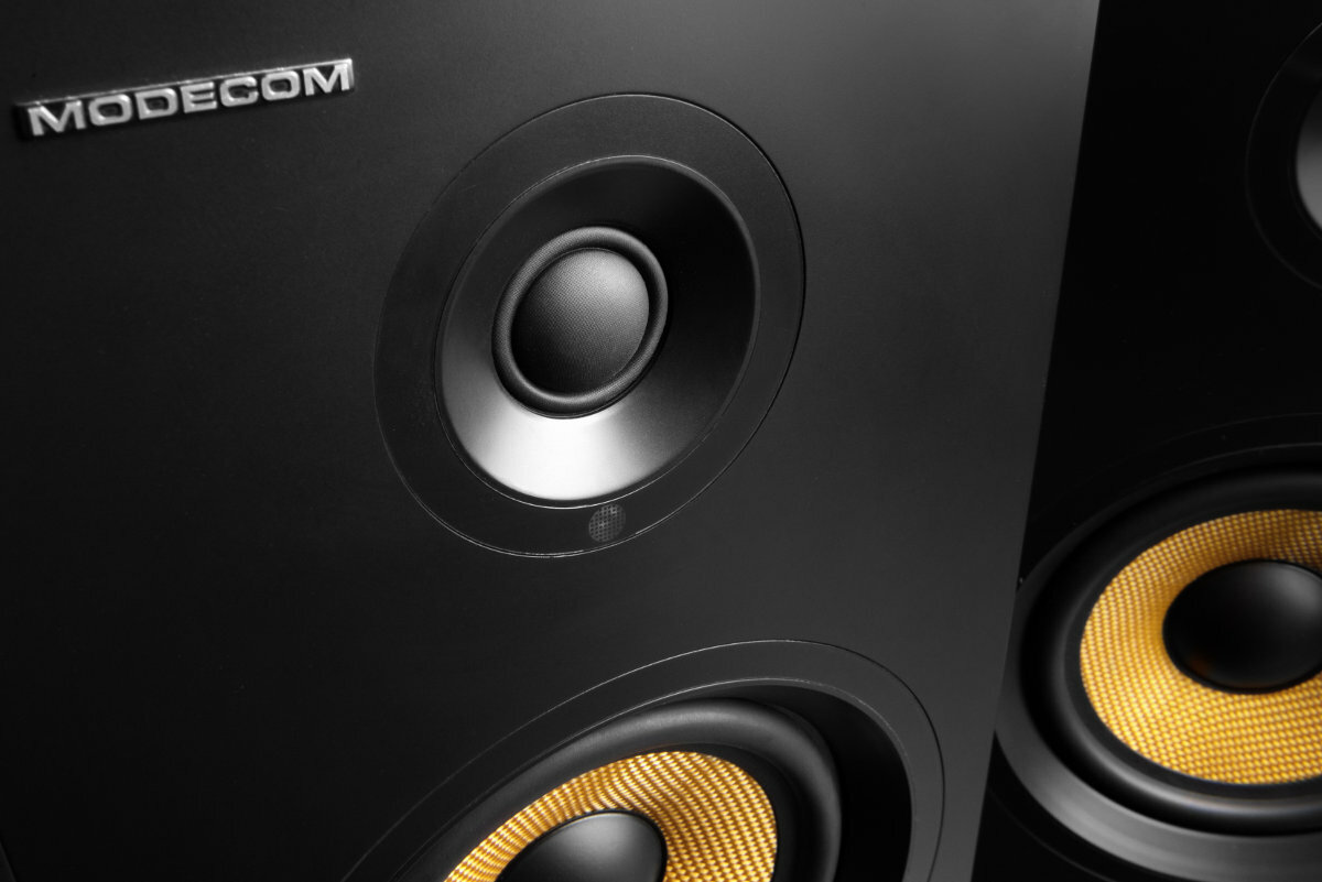 Czarny głośnik z logo Modecom i żółtymi stożkami głośnikowymi.