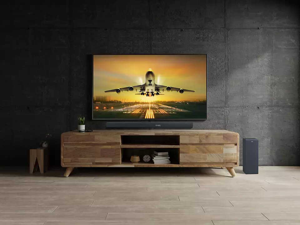 Pokój z telewizorem, soundbarem, szafką i małym głośnikiem.