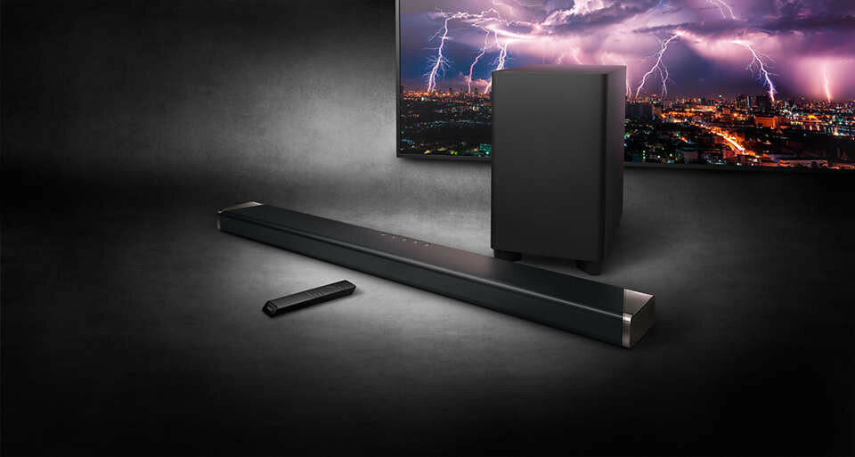 Soundbar, subwoofer i pilot na ciemnej powierzchni, z telewizorem pokazującym błyskawice.