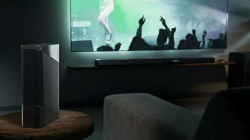 Scena w salonie z głośnikiem, telewizorem i soundbarem. Na ekranie widoczna jest sylwetka osoby.