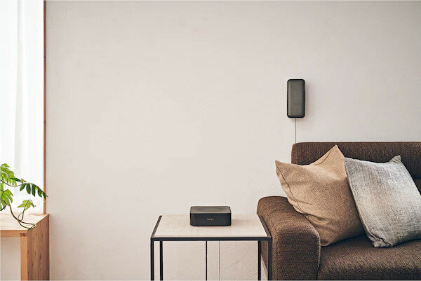 Mały czarny głośnik na stole, wysoki głośnik na ścianie i kanapa.