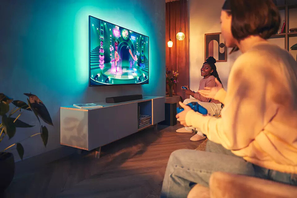 Dwie osoby grające w gry wideo na telewizorze, z soundbarem poniżej.
