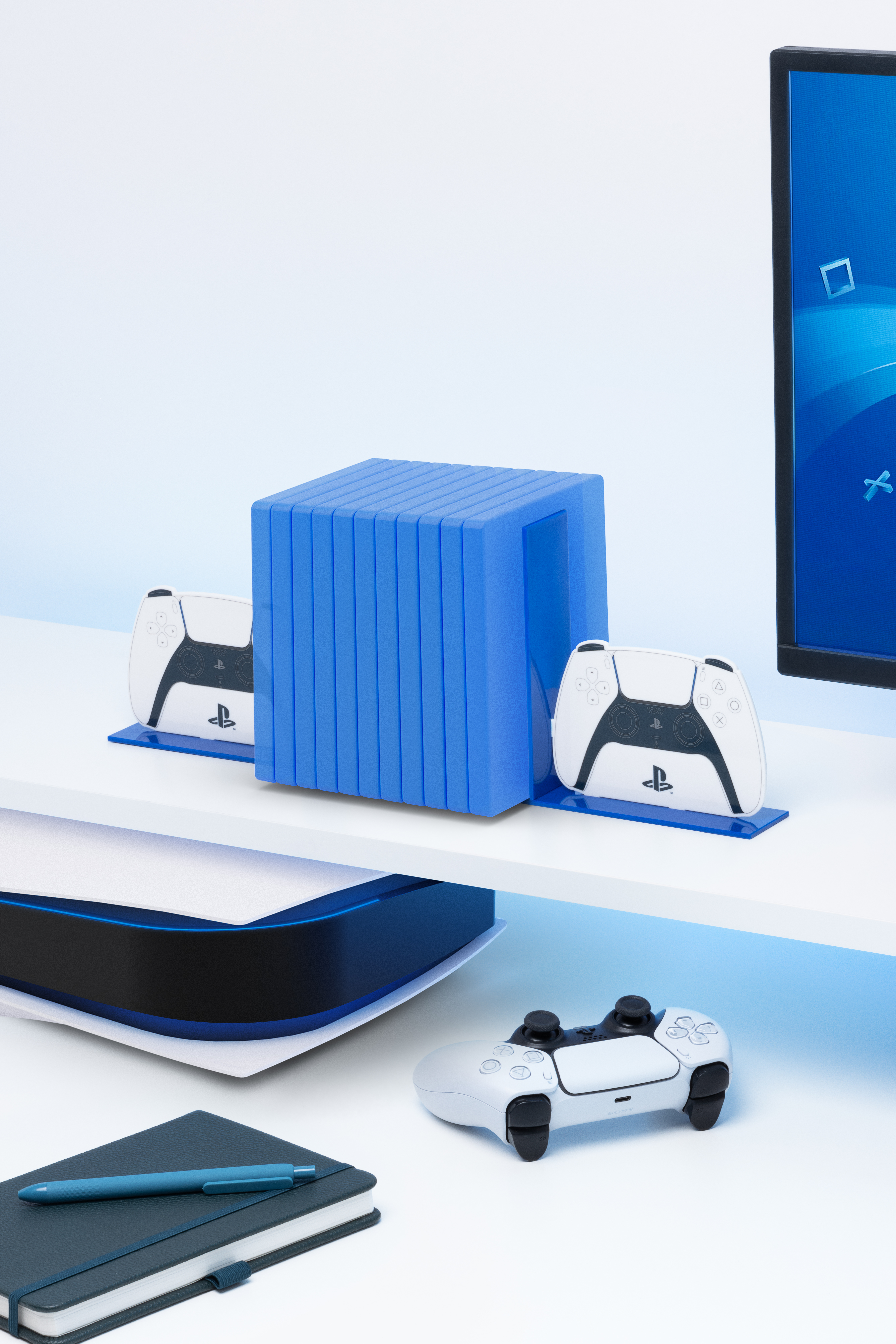 Ein weißer Schreibtisch mit blauem Ständer, PS5-Controllern und einem Monitor.