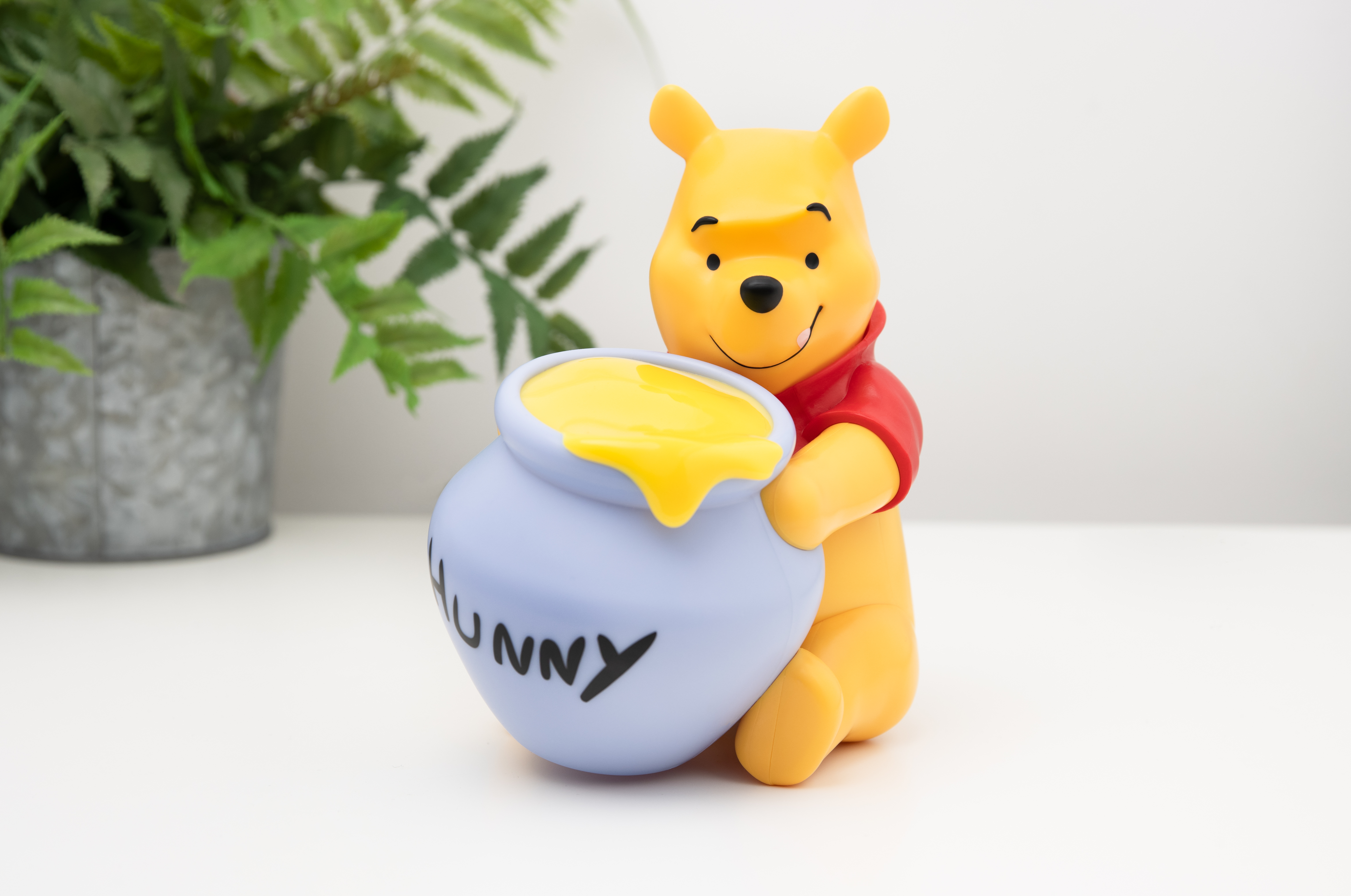 Winnie Puuh Figur mit Honigtopf, gelbem Honig, auf weißer Oberfläche.