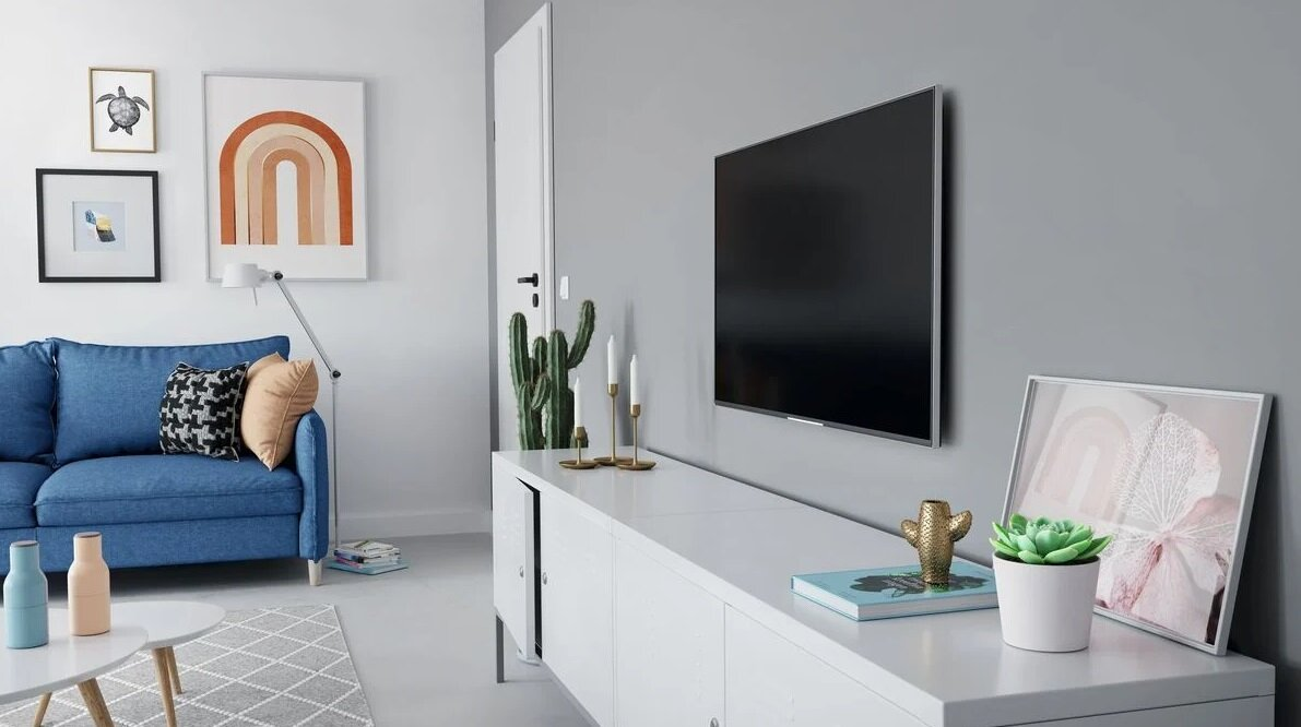 Salon z niebieską sofą, dziełami sztuki, białą szafką, TV i dekoracjami.