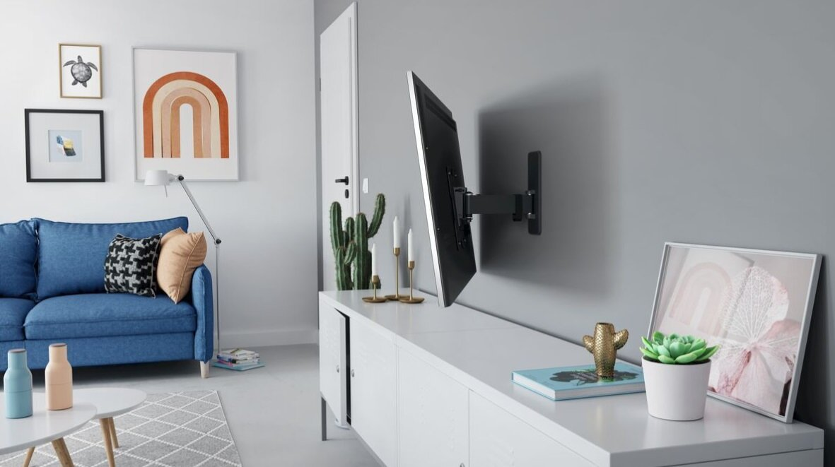 Salon z niebieską sofą, telewizorem na ścianie, obrazami, białą szafką i elementami dekoracyjnymi. Jasna i przestronna atmosfera.