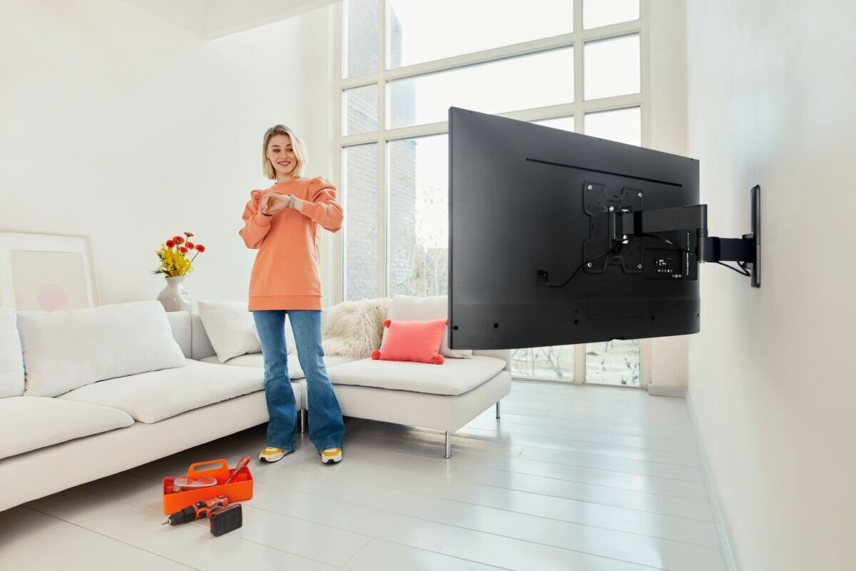 Kobieta w pokoju z telewizorem na ścianie. Dopasowuje zegarek. Narzędzia na podłodze.