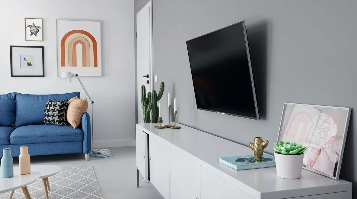 Salon z telewizorem na ścianie, niebieską kanapą i dziełami sztuki. Są też rośliny i stolik kawowy.