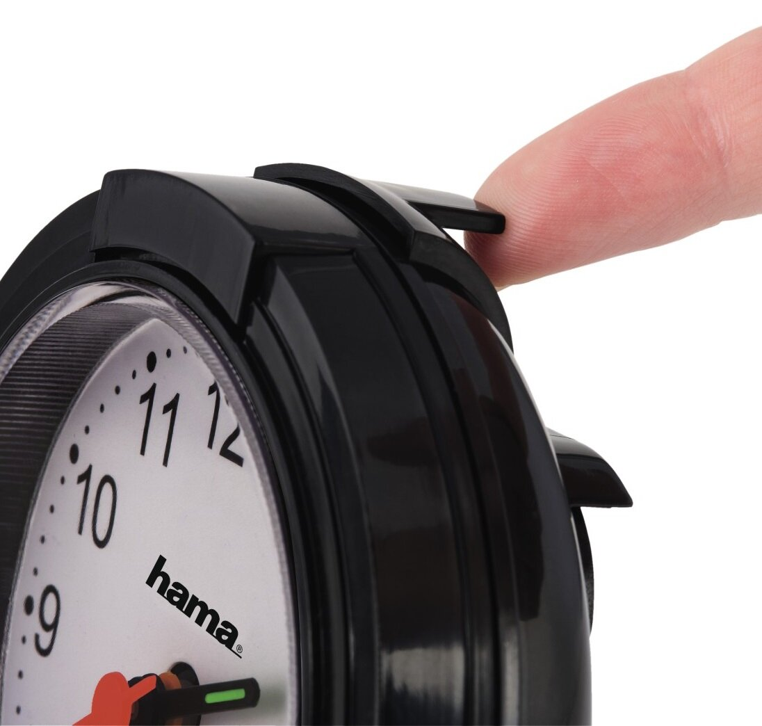 Czarny budzik analogowy. Palec naciska górny przycisk. Biała tarcza zegara.