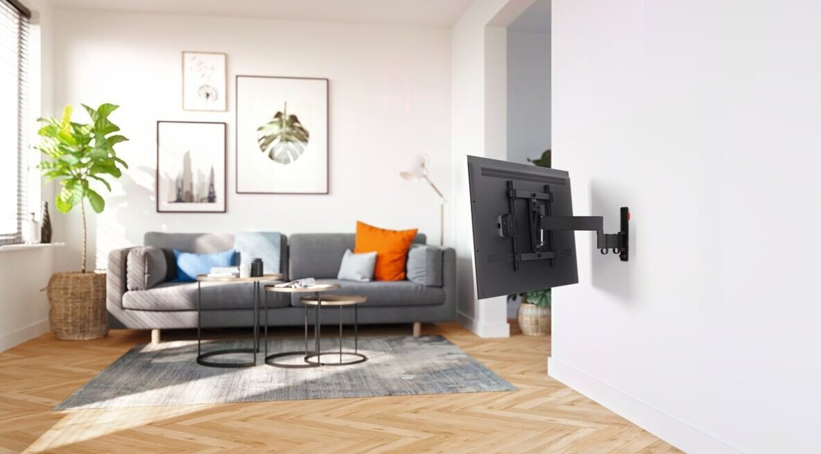 Telewizor zamontowany na ścianie w salonie. Widoczna sofa, stolik kawowy i roślina.