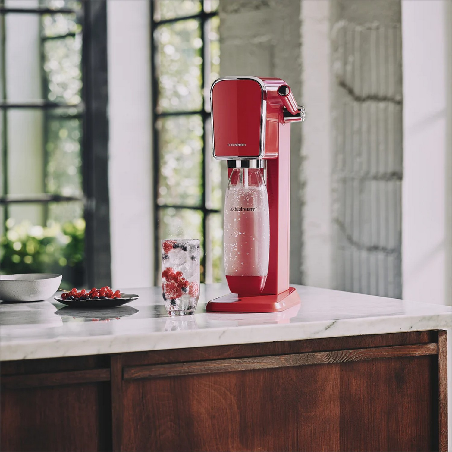 Machine à soda rouge avec un verre de baies et de soda sur un comptoir blanc.