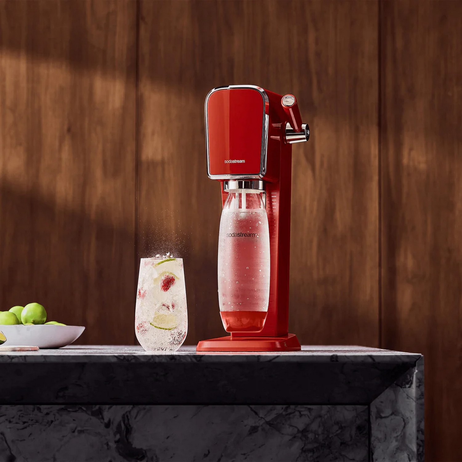 Machine SodaStream rouge avec un verre d'eau gazeuse et des fruits, sur une surface en marbre.