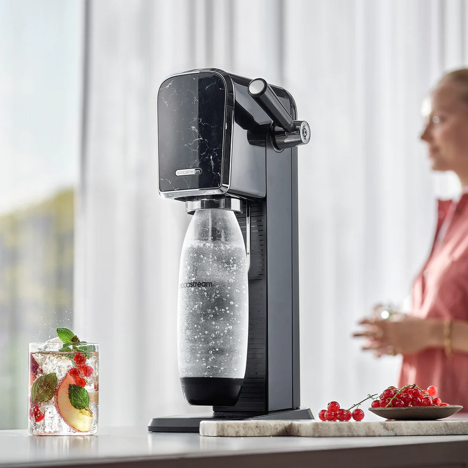 A soda maker with a glass of beverage and ingredients.