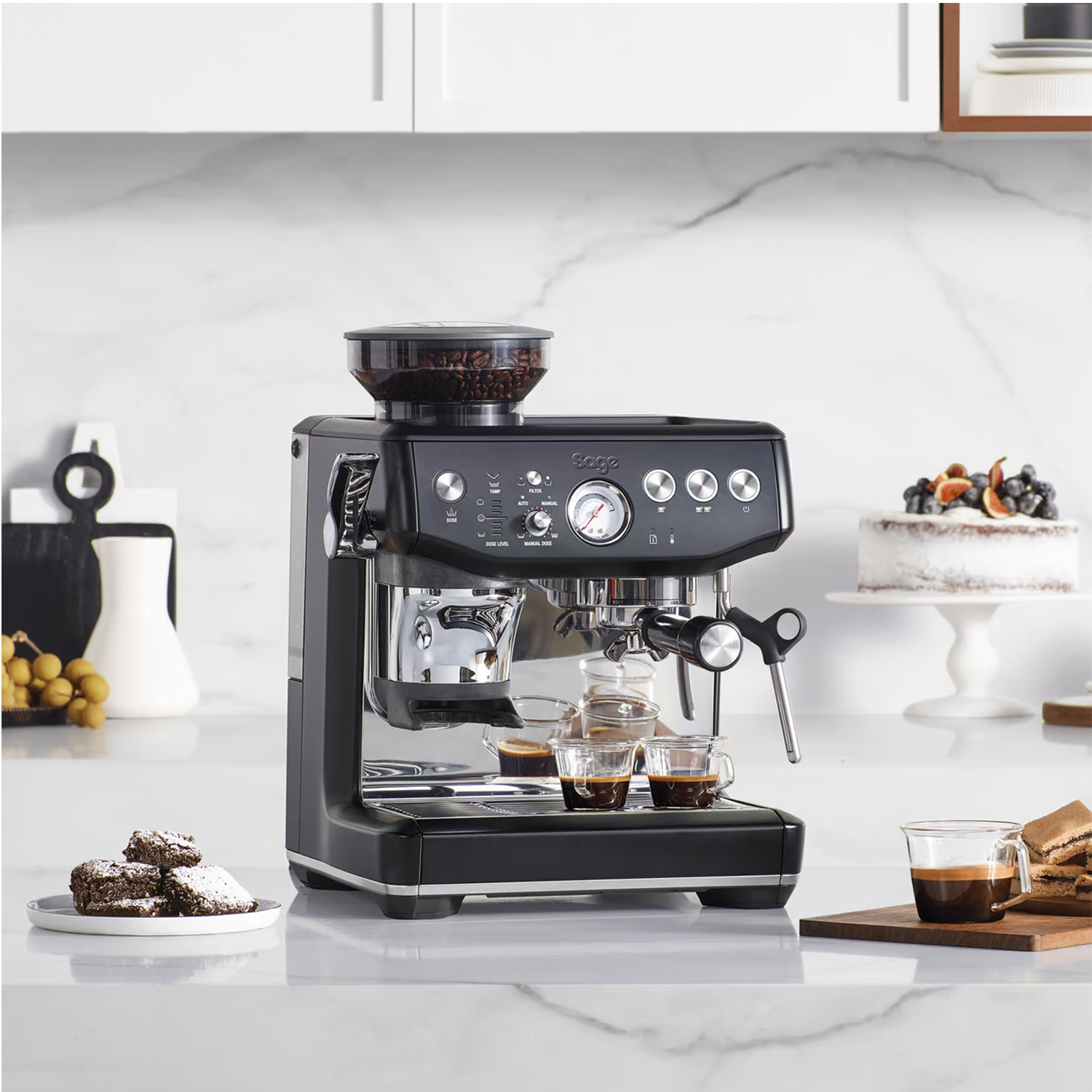 Macchina per espresso su un bancone. Ha un macinacaffè, un portafiltro e una lancia a vapore. Una torta è sullo sfondo.