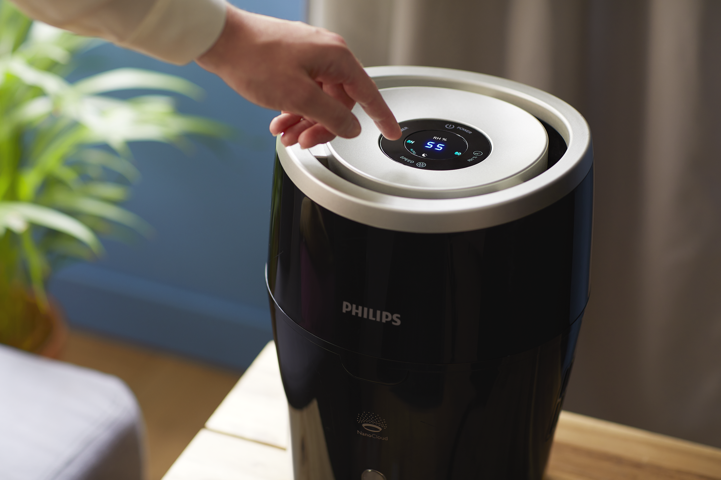 Palec osoby dotyka panelu sterowania czarnego nawilżacza Philips, ustawionego na drewnianym stole.