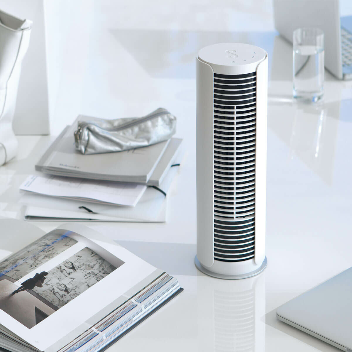 Biały wentylator wieżowy na białym biurku z przedmiotami wokół. Białe tło.
