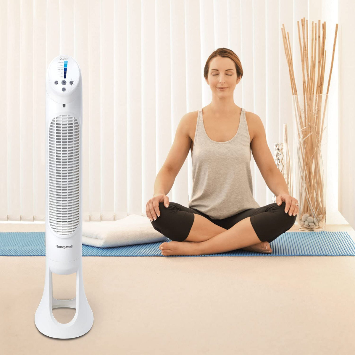 Kobieta medytuje obok wentylatora i wazonu z patykami.