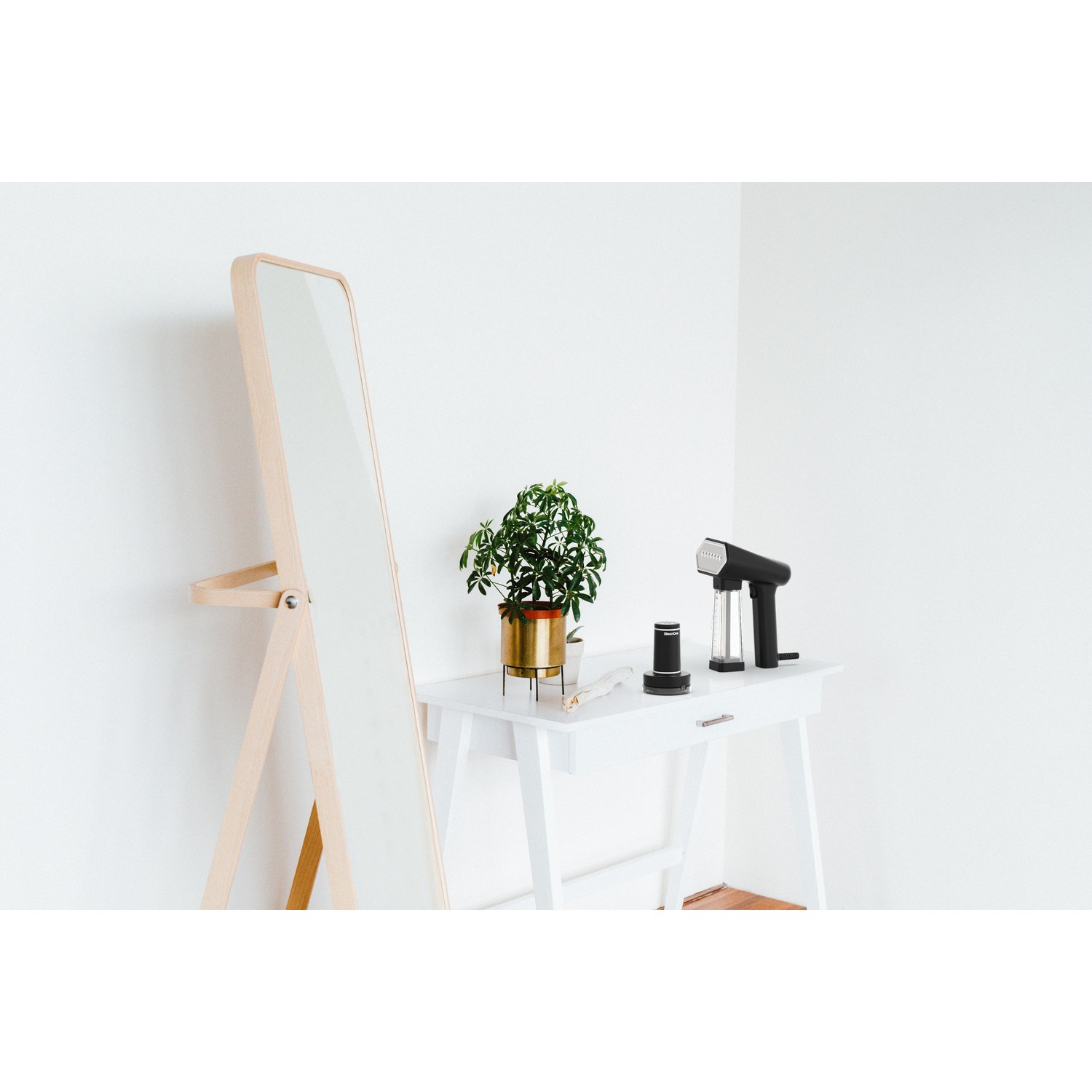 Une table blanche avec miroir, plante en pot doré et produits coiffants sur un mur blanc.