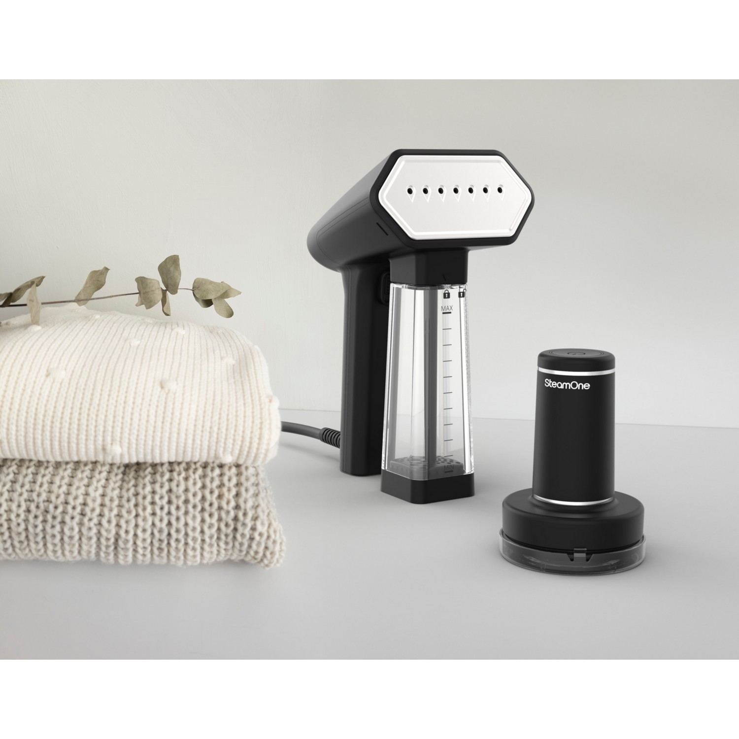 Un défroisseur de vêtements noir et blanc à côté de vêtements pliés et d'une base SteamOne.