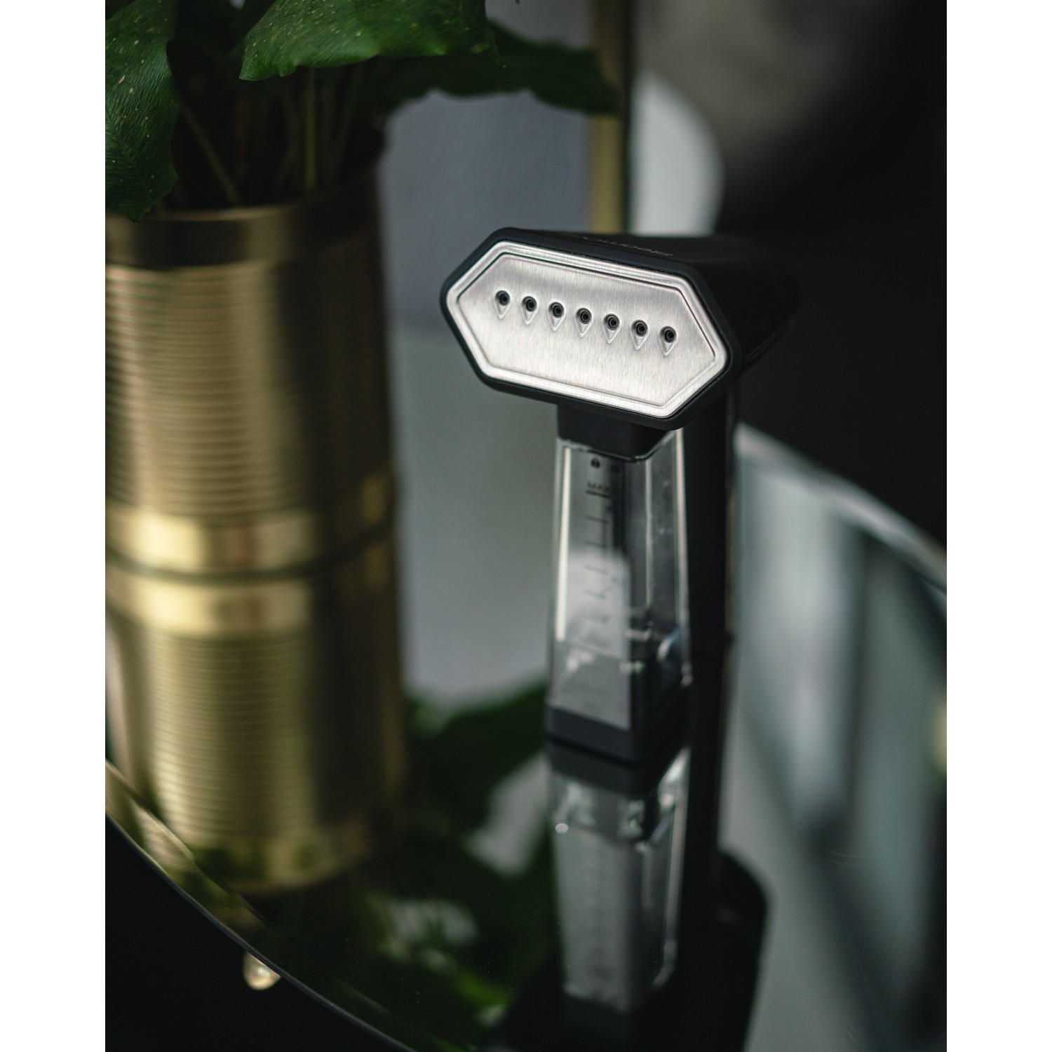 Vapeur de vêtements noir et argent. Il a un réservoir d'eau transparent et est sur une surface en verre.