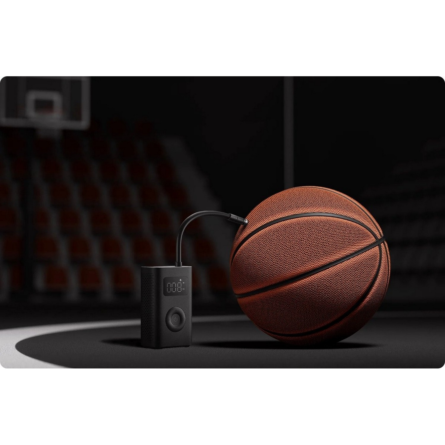 Une pompe à air noire est connectée à un ballon de basket. Scène : terrain de basket avec un panier en arrière-plan.