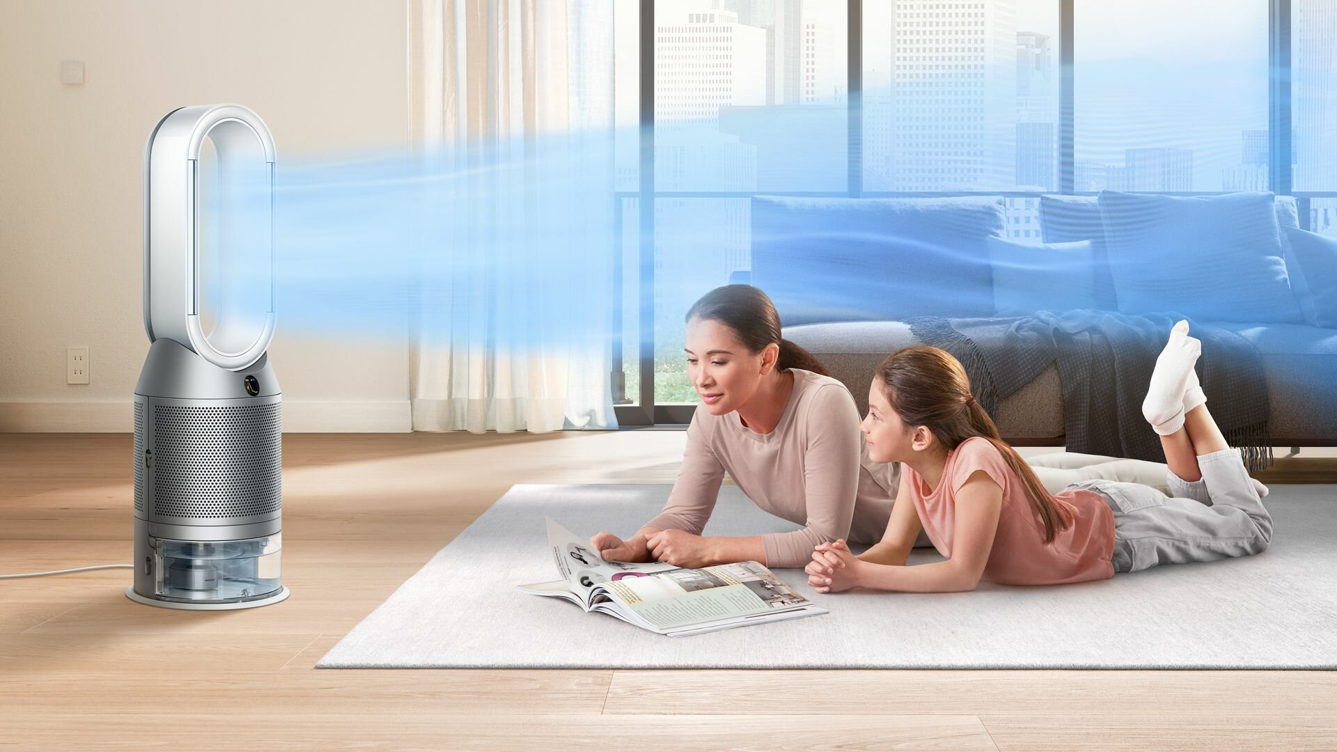 Matka i córka czytają na dywanie, obok wentylatora, który wydmuchuje niebieski strumień powietrza.
