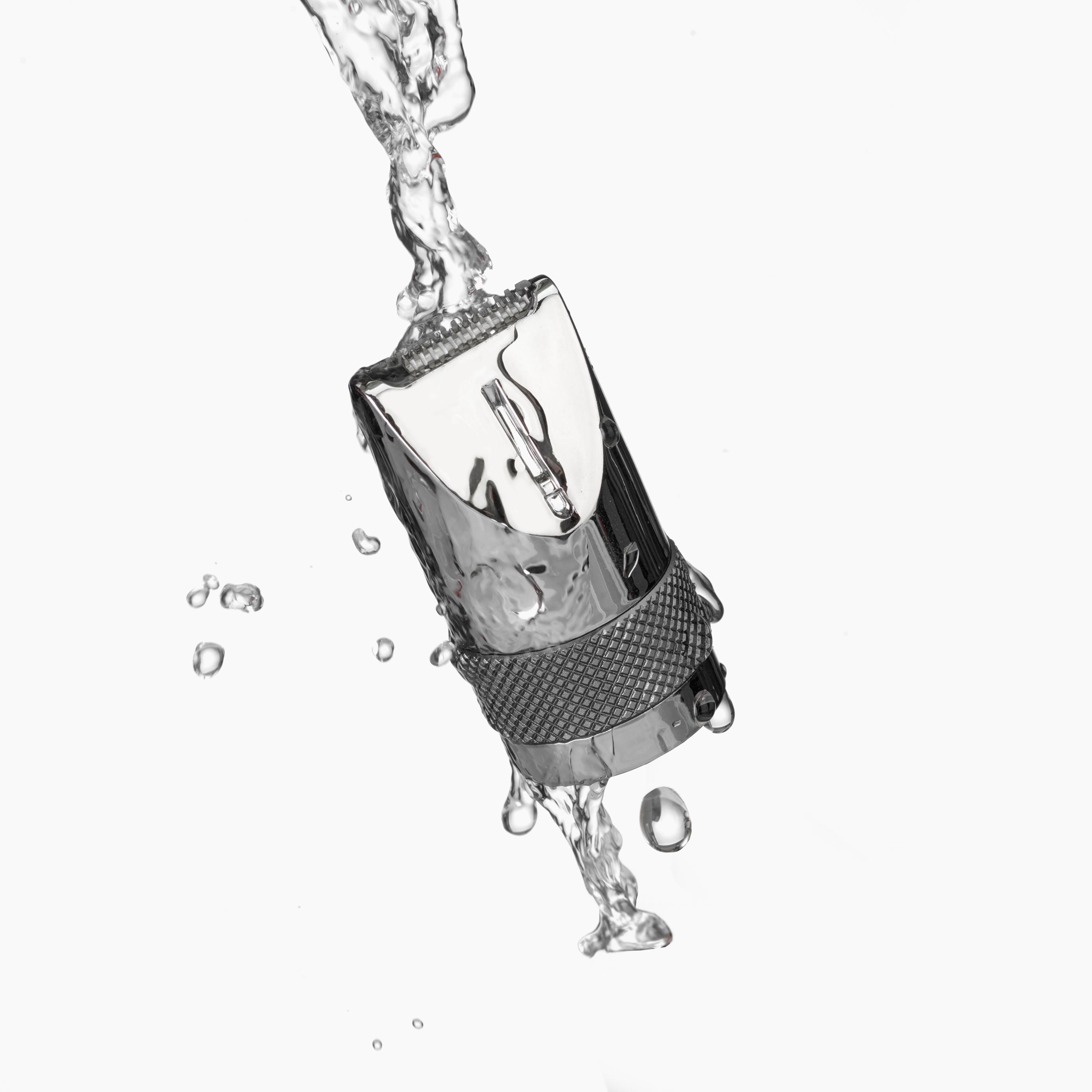 Ein chromfarbener Elektrorasierer hängt im Wasser, mit Spritzern und Tropfen drumherum auf weißem Hintergrund.
