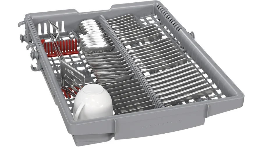 Koszyk zmywarki z przyborami. Sztućce, biały kubek i czerwony uchwyt na przybory są w nim.