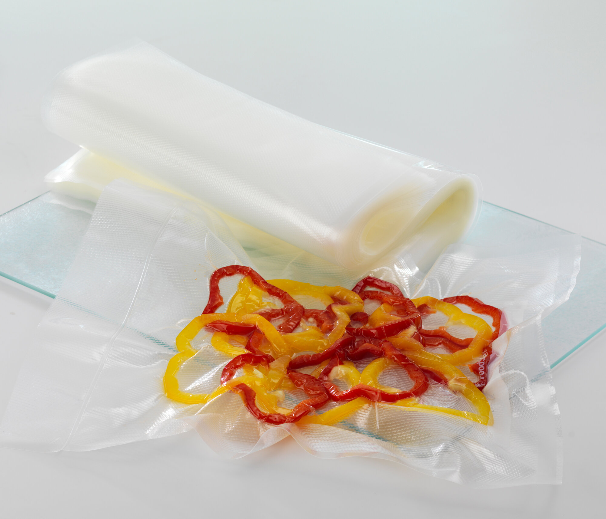 Krojona czerwona i żółta papryka w worku próżniowym. Inne worki zwinięte. Białe tło.