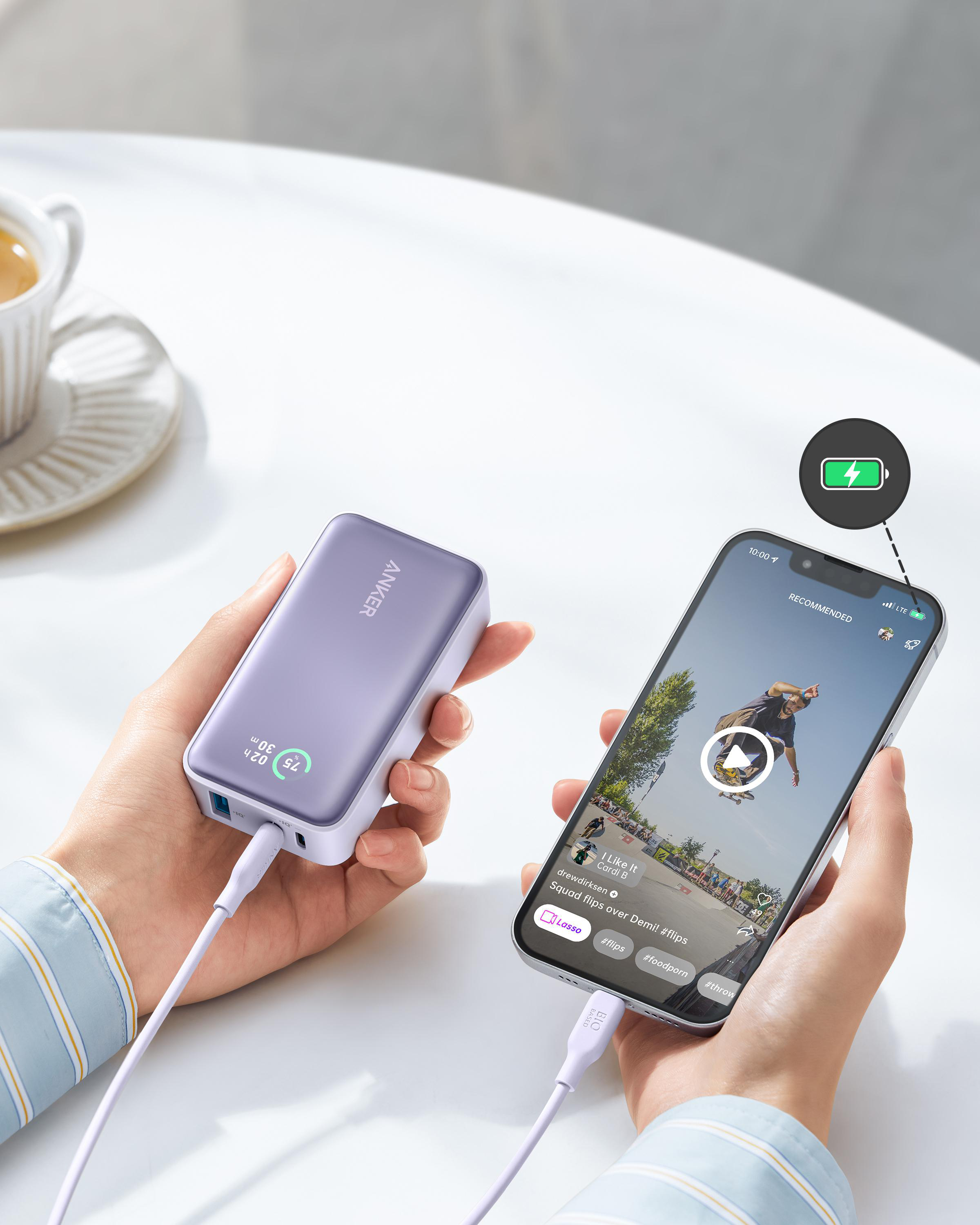 Hände halten Anker Powerbank, die ein Video abspielendes Telefon lädt.