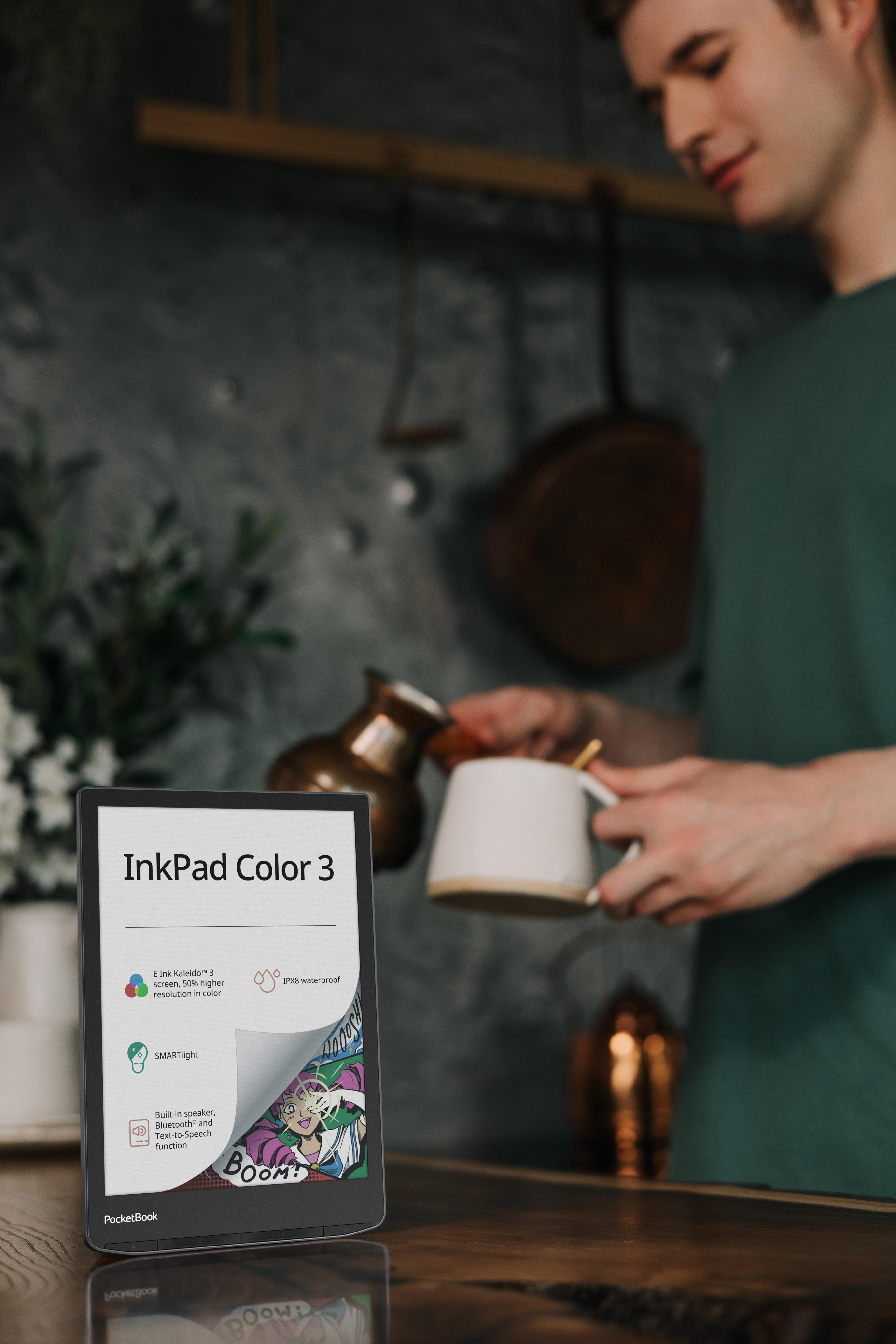 Person hält Tasse in der Nähe eines Tisches mit E-Reader und bunter Illustration.