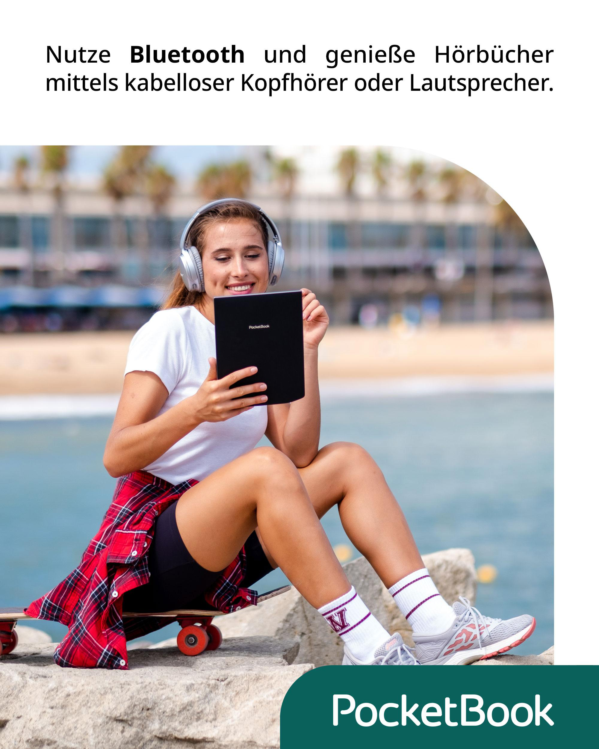 Frau mit Kopfhörern benutzt ein Tablet auf einer Steinmauer am Strand.