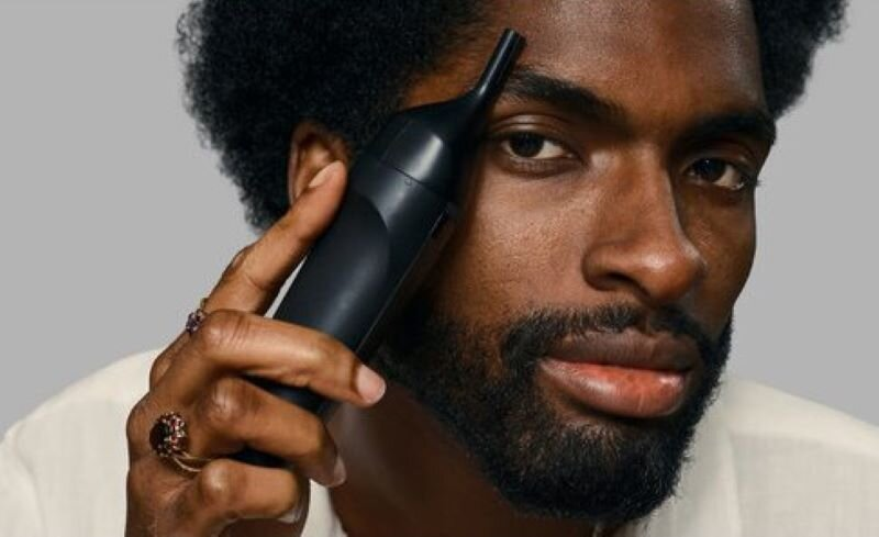 Czarny mężczyzna z brodą używający urządzenia do pielęgnacji twarzy.