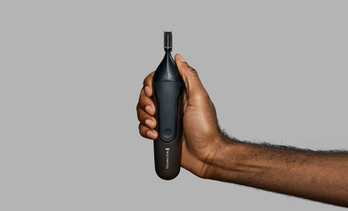 Mężczyzna trzymający czarny trymer do włosów w nosie Remington na szarym tle.