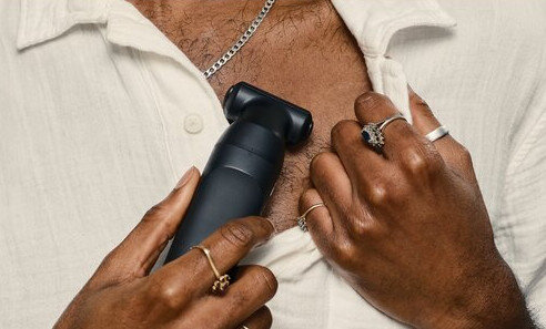 Osoba goli włosy na klatce piersiowej czarną elektryczną maszynką.