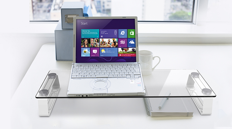 Laptop üvegtartón, jegyzettömb, toll és bögre mellett. Windows 8 felület látható. Fehér háttér.