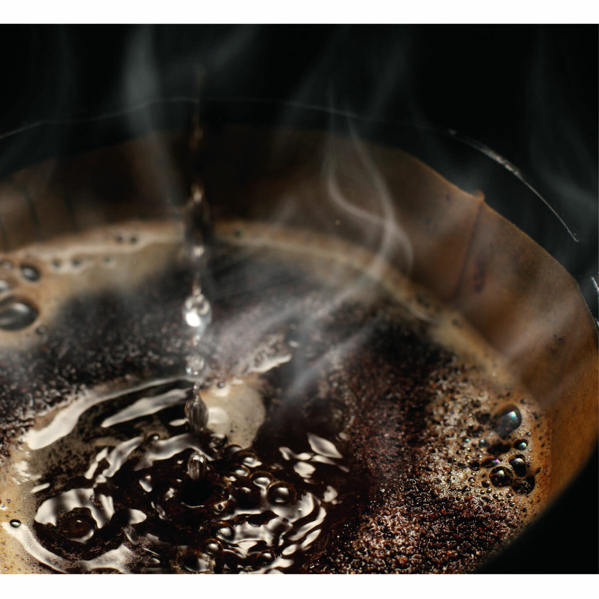 Woda kapie do filtra z fusami kawy. Para unosi się na czarnym tle.