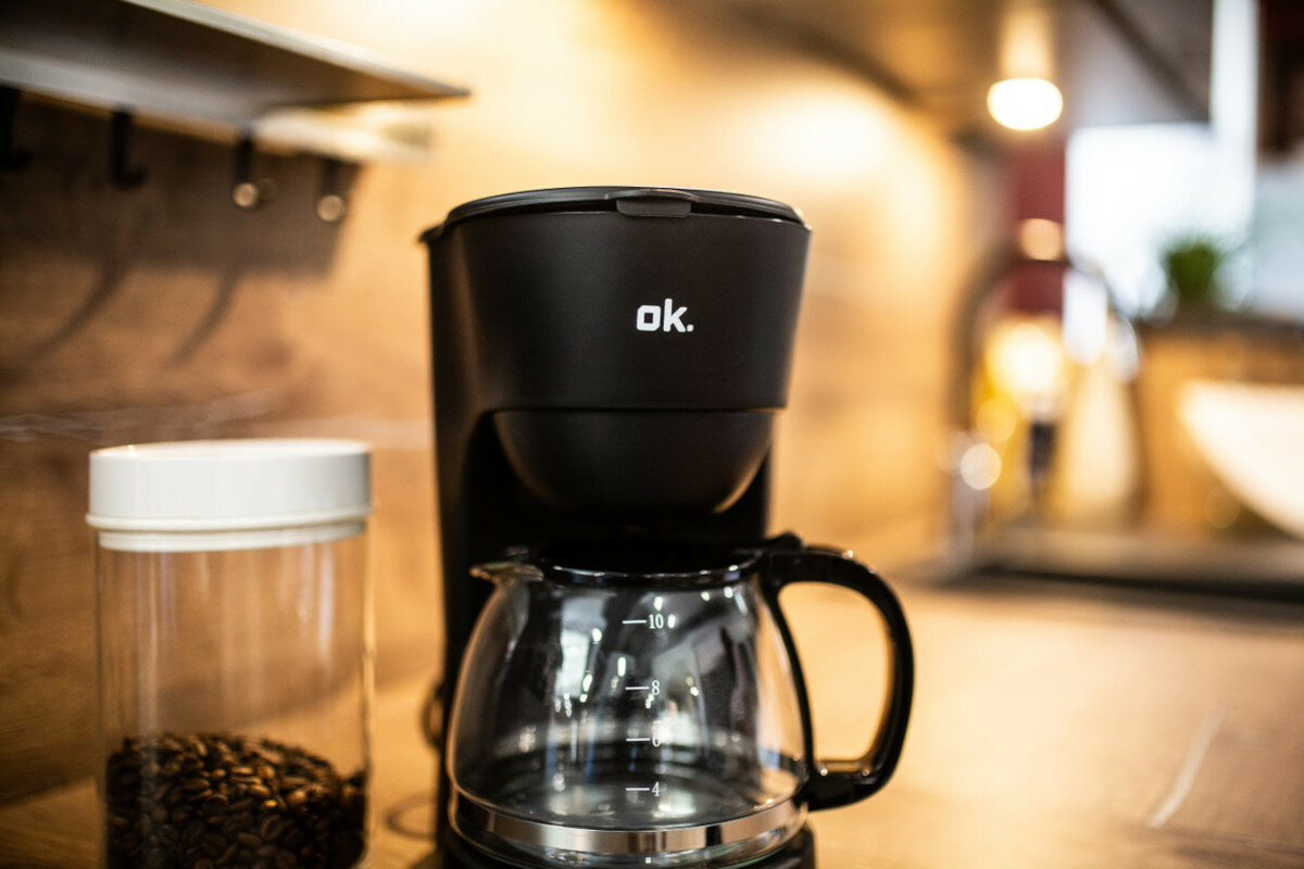 Czarny ekspres do kawy ze szklaną karafką i ziarnami kawy w słoiku.