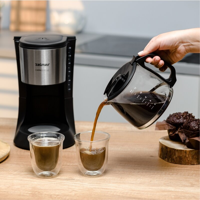 Ekspres do kawy nalewa kawę do dwóch szklanek, muffiny w tle.