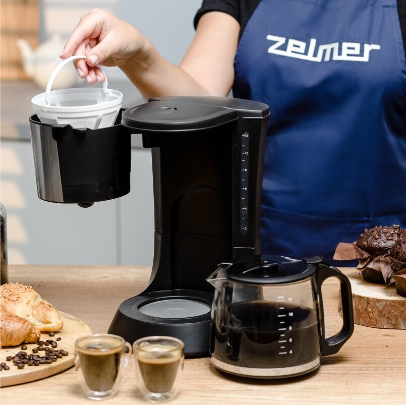 Osoba przygotowuje kawę w czarnym ekspresie do kawy, obok ciasta.